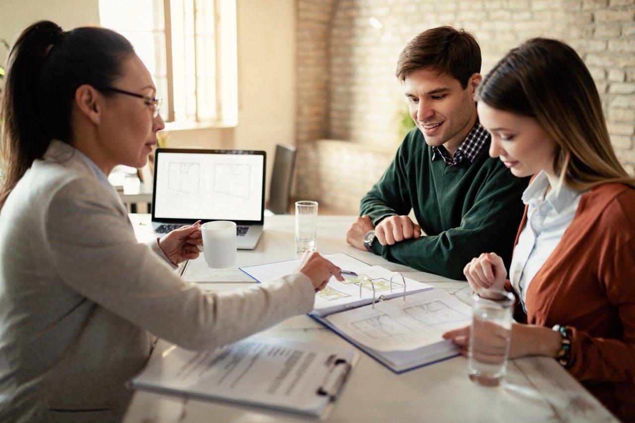 Smiling couple and insurance agent going through real estate plans during a meeting in the office. Focus is on man.